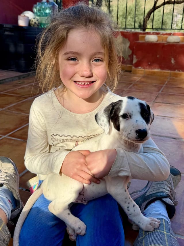 Amaiya grinning at the camera with Patch as a puppy cradled on her lap.