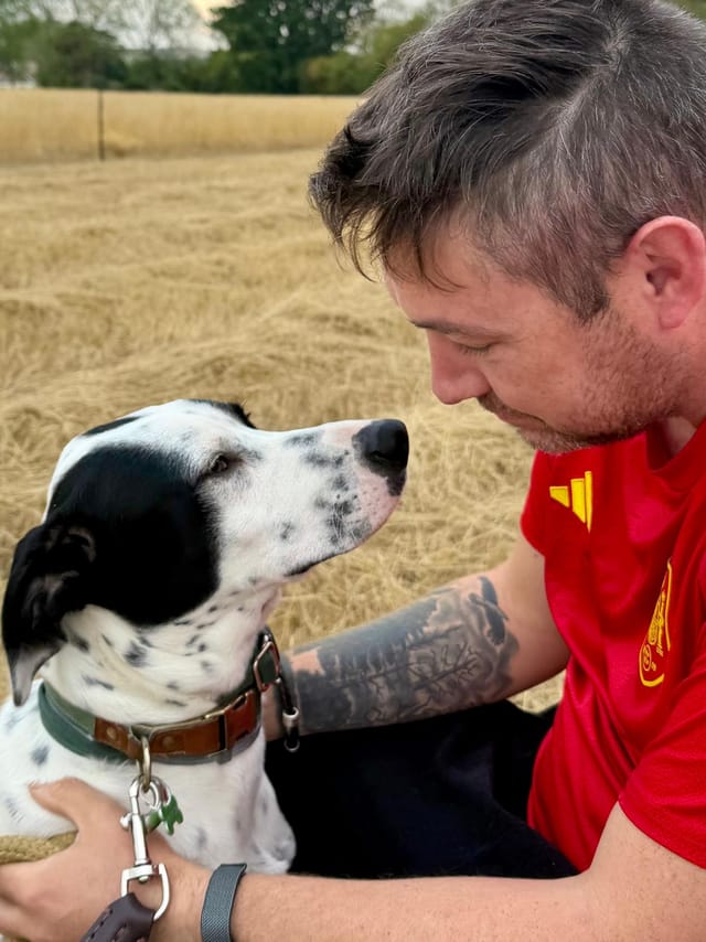 Callum sitting in a stubble field, nose to nose with Patch.