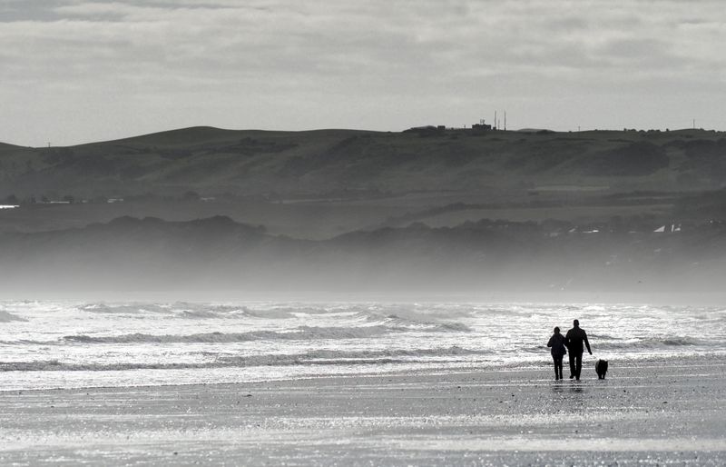 A couple and their dog in silhouette, walking along a wide, misty beach at Filey beside breaking waves.